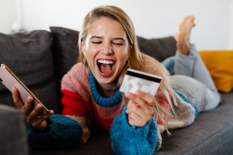 mulher deitada no sofá radiante de felicidade segurando um cartão de crédito
