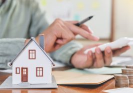 homem fazendo conta na calculadora e destacado a frente a imagem de uma casa