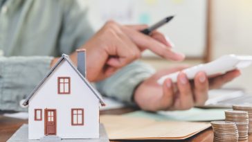 homem fazendo conta na calculadora e destacado a frente a imagem de uma casa