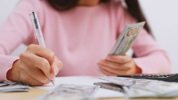 mulher fazendo anotações e na outra mão segurando dinheiro