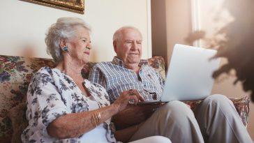 casal de idosos usando o computador sentados na sala