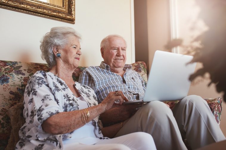 casal de idosos usando o computador sentados na sala
