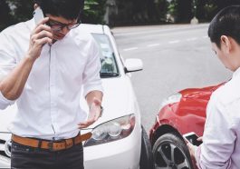 Dois homens envolvidos em acidente de trânsito, um falando ao celular e outro acessando a internet