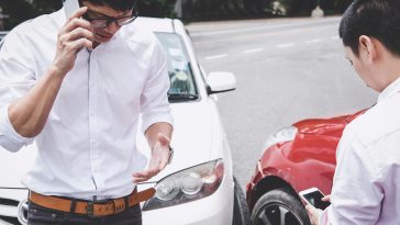 Dois homens envolvidos em acidente de trânsito, um falando ao celular e outro acessando a internet