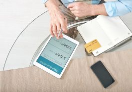 mão masculina mexendo em tablet escrito banco online ao lado de um caderno com cartão de crédito