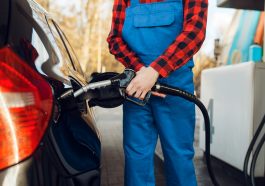 frentista de uniforme azul segurando a bomba de gasolina para encher o tanque de um carro