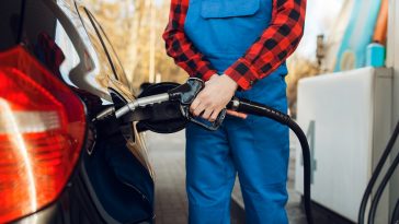 frentista de uniforme azul segurando a bomba de gasolina para encher o tanque de um carro