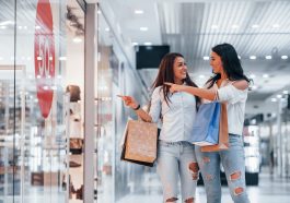 duas mulheres apontando uma vitrine de shopping com a indicação de 50% de desconto