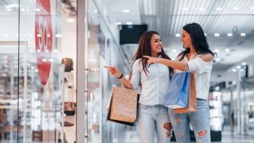 duas mulheres apontando uma vitrine de shopping com a indicação de 50% de desconto