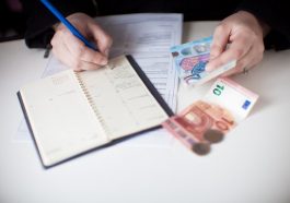mão de mulher anotando gastos em um papel e dinheiro na volta