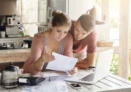 casal jovem lendo um documento em frente ao computador
