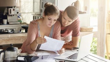 casal jovem lendo um documento em frente ao computador