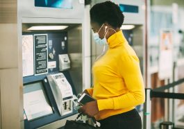 Mulher africana vestindo uma máscara protetora retira dinheiro de um cartão bancário