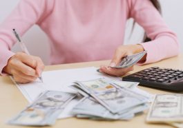 mulher fazendo e anotando contas ao lado de dinheiro e calculadora