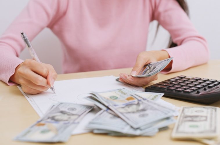 mulher fazendo e anotando contas ao lado de dinheiro e calculadora