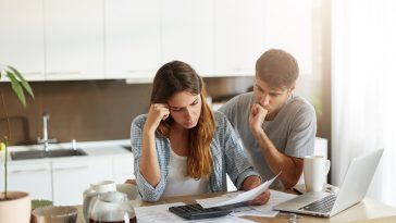 Casal de família triste percebendo suas dívidas com cheque especial, olhando atentamente em documentos, calculando sua família