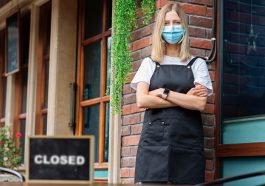mulher de máscara em frente à um restaurante com a placa de fechado, indicando a crise de desemprego no Brasil