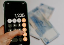 mão de mulher calculando conta na calculadora do celular e notas de dinheiro ao fundo