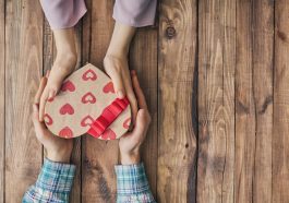 mão de casal de namorados segurando uma caixa de coração de presente, simbolizando as compras no comércio mineiro no dia dos namorados