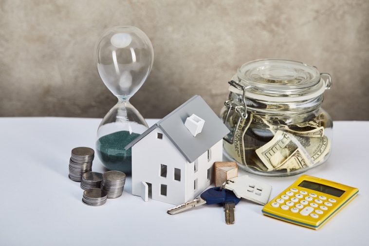 modelo de casa com ampulheta, calculadora, dinheiro e chaves, conceito imobiliário