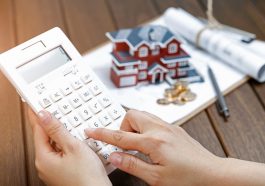 mão feminina operando uma calculadora na frente de um modelo de casa simbolizando a inflação do aluguel no Brasil