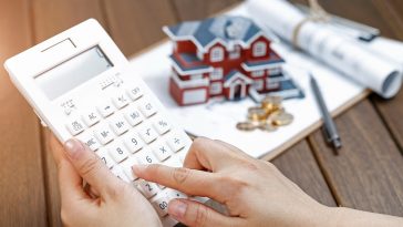 mão feminina operando uma calculadora na frente de um modelo de casa simbolizando a inflação do aluguel no Brasil