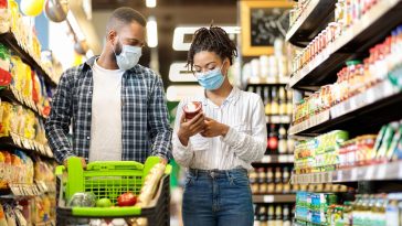 Casal afro-americano em máscaras comprando mantimentos comida no supermercado, simbolizando o preço da cesta básica no Brasil em Junho