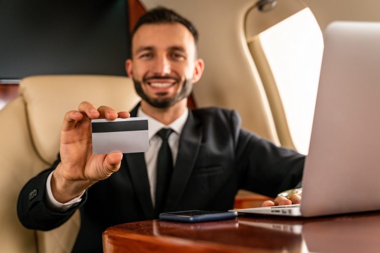homem de terno em avião sentado exibindo seu cartão de crédito de alta renda