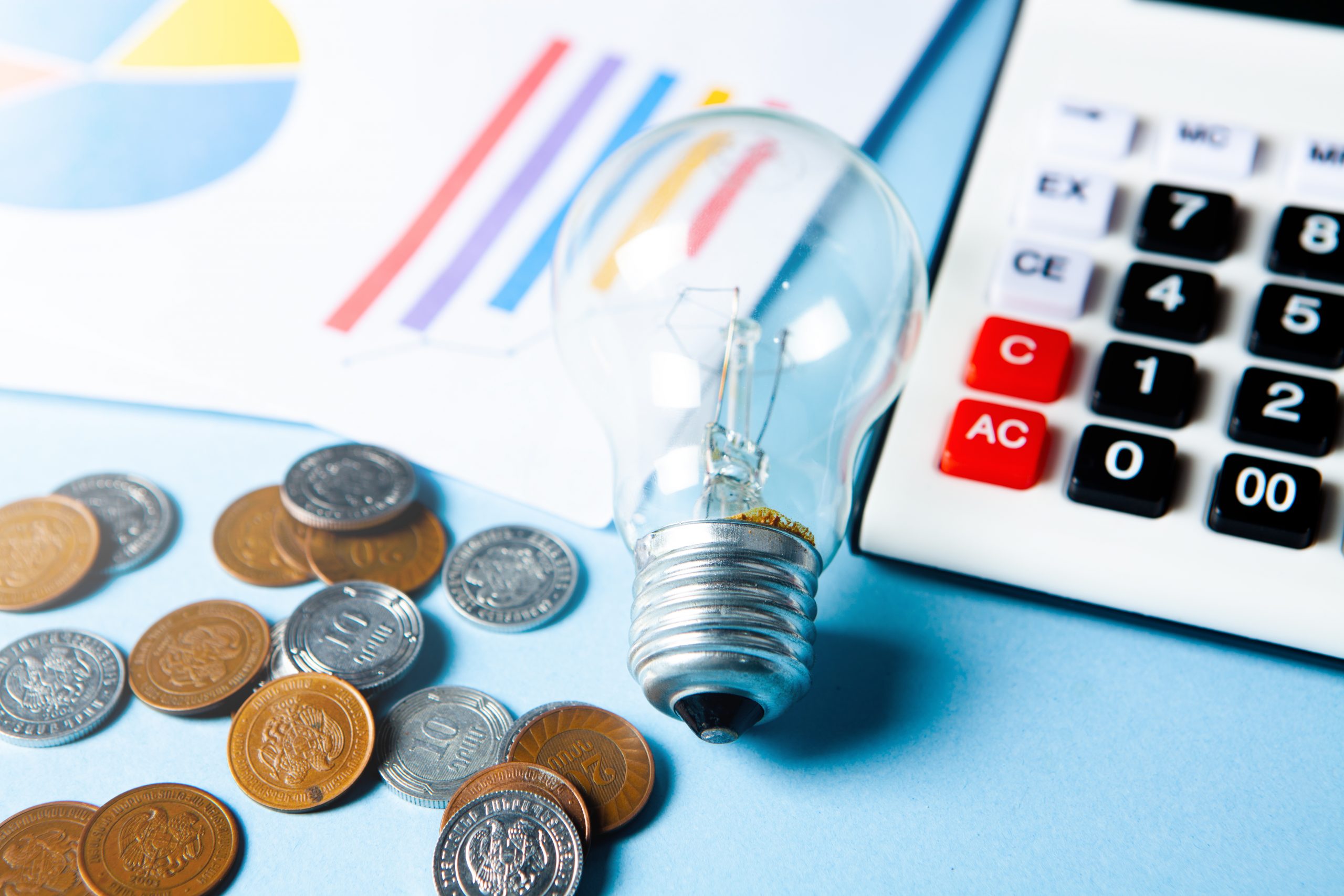 lâmpada em cima de uma mesa e na volta algumas moedas e calculadora representando a nova bandeira tarifária aumento conta de luz