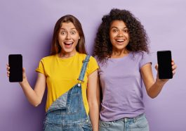 dois adolescentes multiétnicos sorridentes se aproximam, mostram smartphones com telas de maquete para seu texto sobre como escolher o celular ideal