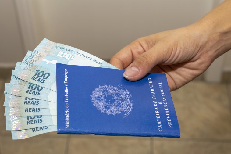 carteira de trabalho com dinheiro notas de cem reais dentro demostrando as novas vagas de emprego no Brasil