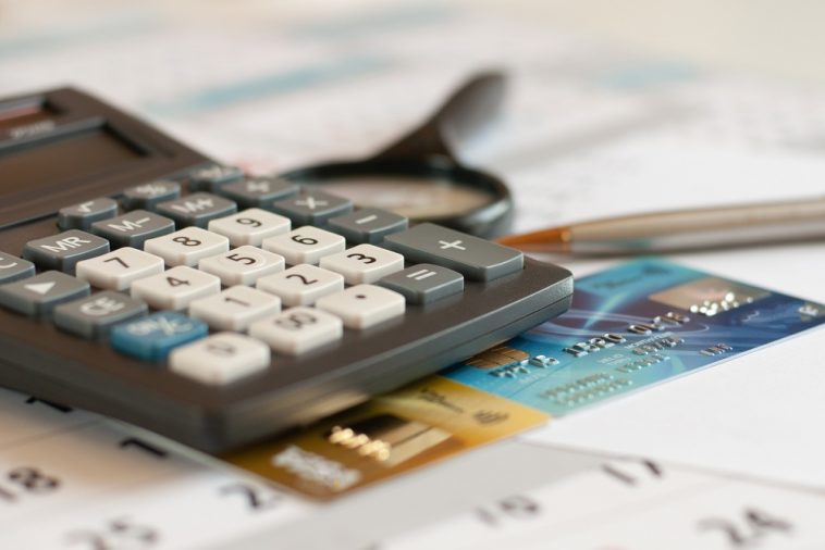 imagem de calculadora, lupa sobre contas e dois cartões de crédito ao lado simulando oparcelamento com cartão de crédito