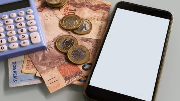 calculadora, notas de 10,00 reais e um celular na mesa simbolizando como diminuir gastos em casa para economizar
