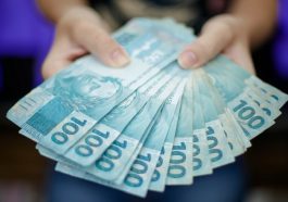 mão de mulher segurando várias notas de cem reais abertas em formato de leque