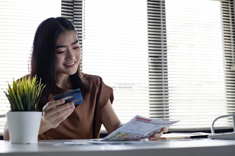 Jovem mulher asiática segurando o cartão de crédito e a conta com um sorriso na mesa de trabalho em casa. mulheres sorriem felizes depois de não ter dívidas. não se preocupa com os problemas causados pela dívida do cartão de crédito