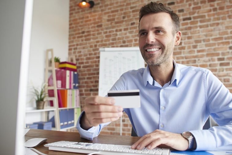 Homem focado enquanto trabalha no computador com seu cartão de crédito MEI