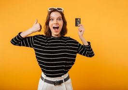 Retrato de uma menina feliz, segurando o cartão de crédito indicando os melhores cartões para 2022