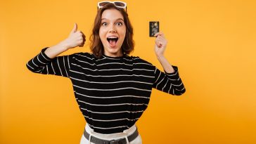 Retrato de uma menina feliz, segurando o cartão de crédito indicando os melhores cartões para 2022