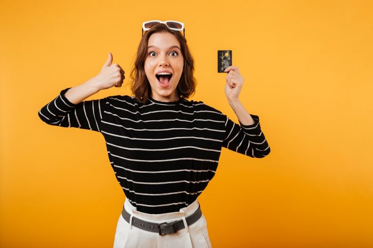 Retrato de uma menina feliz, segurando o cartão de crédito indicando os melhores cartões para 2022