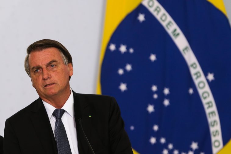 bolsonaro falando e ao fundo uma bandeira do Brasil