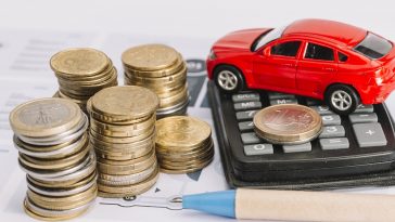 Pilha de moedas; calculadora; carro de brinquedo e caneta no modelo simulando o IPVA mais caro em 2022