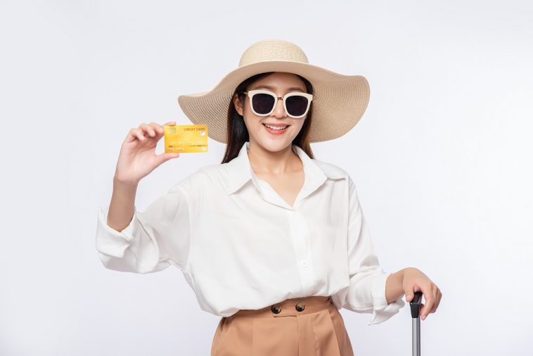 Menina de chapéu segurando um cartão de crédito e uma mala para viajar , simbolizando como viajar de graça usando cartão ao abastecer