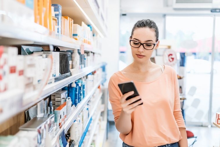 moça mexendo no celular em uma farmácia, simbolizando Bandeira Elo está oferecendo descontos de até 75% em farmácias