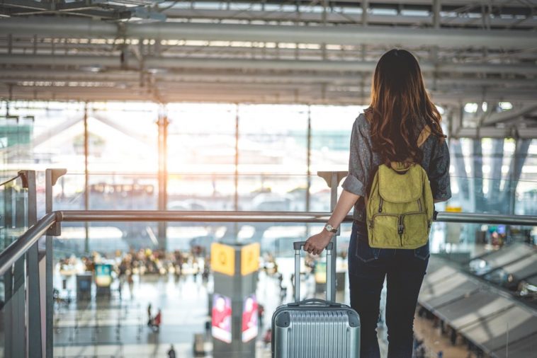Turista esperando com mala na mão, olhando voo para decolar no aeroporto