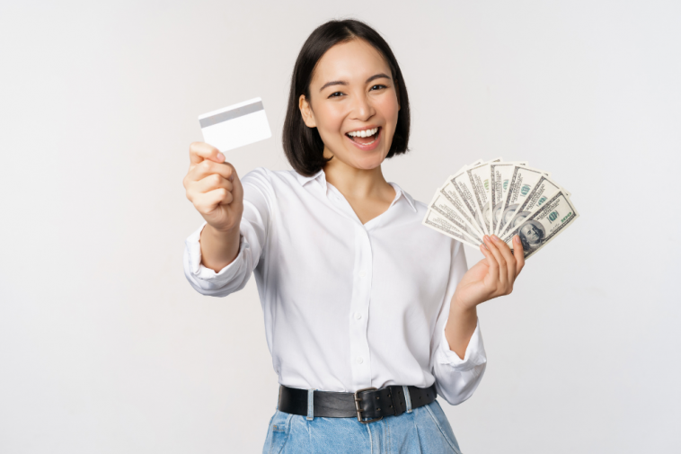 mulher coreana feliz e sorridente segurando cartão em uma mão e na outra notas de dólar, simbolizando como ganhar dinheiro com o cartão de crédito