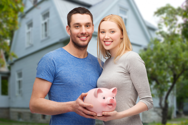 casal jovem feliz segurança cofrinho de porquinho ao fundo de uma casa, simbolizando Como juntar dinheiro em casal